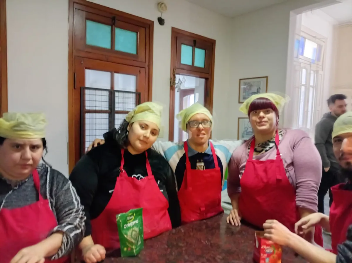 Concurrentes del taller de cocina con delantales rojos y gorros, posando en la cocina del centro